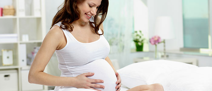 woman who is pregnant holding her stomach, as if she is wanting feel the baby kicking