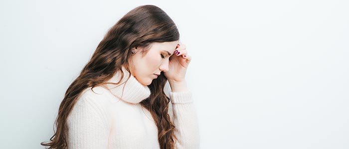 woman in white sweater holding her head as if she is dizzy