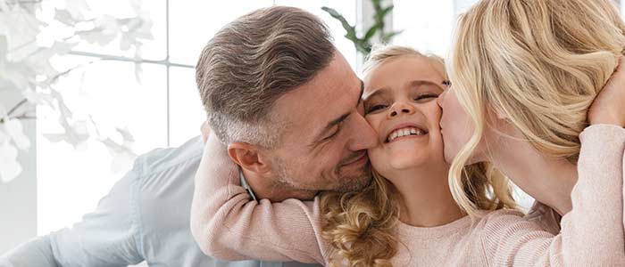 Girl child getting hugs from both mom and dad